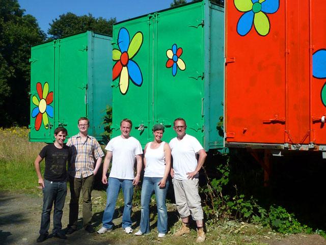 Vier Männer und eine Frau vor bunten Containern