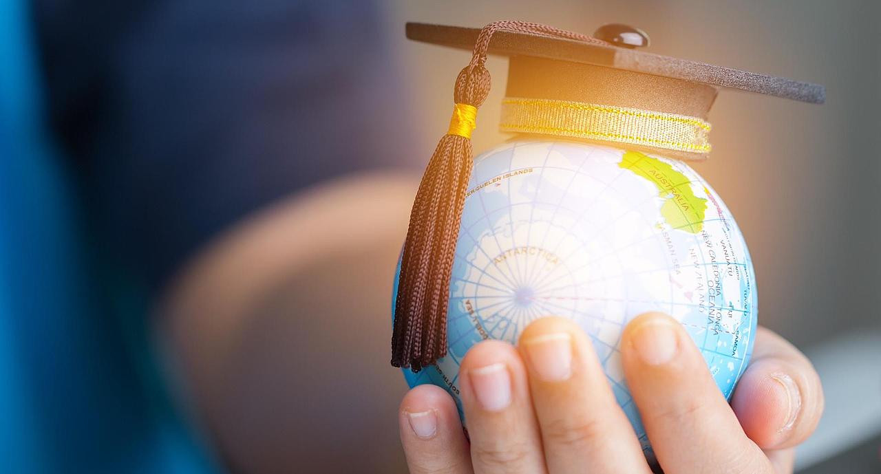 Hand hält Globus mit Doktorhut