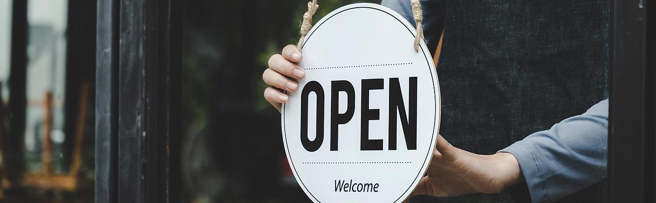 Person hält Türschild mit Aufschrift "Open"