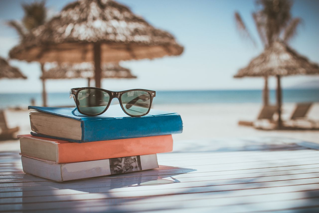 Brille auf Bücherstapel vor tropischem Hintergrund