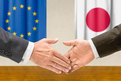 Handschlag vor EU- und Japan-Flaggen